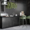 Modern outdoor kitchen with black island, hanging plants, green bar stools, and surrounding greenery.