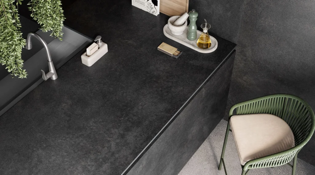Minimalist black kitchen countertop with sink, green chair, hanging plants, and various kitchen accessories.