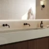 4101_Organic-Dawn_Render2_1282X715_RGB_170226-copy-1024x571 Minimalist bathroom sink with dual black faucets, soap dispenser, towel, and wall-mounted light fixture.