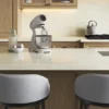 Modern kitchen island with mixer, milk, eggs, two cushioned stools, stovetop, and faucet.
