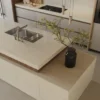 Modern kitchen with marble island, double sink, built-in oven, and decorative plant in vase.