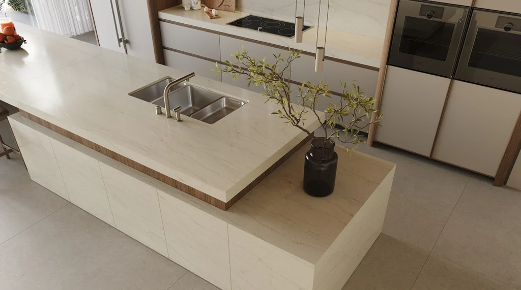 Modern kitchen with marble island, double sink, built-in oven, and decorative plant in vase.