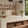 8251_TajWhisper_Render1_1920X1080RGB_050226-1024x576 Minimalist kitchen with wooden shelves, marble island, woven baskets, pendant lights, and greenery outside window.