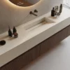 Modern bathroom sink with integrated basin, wooden vanity, round mirror, and grooming accessories.